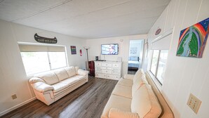 A spacious living room with a beige sofa, a white sofa, a TV mounted on the wall, and a large window. - Rainbow River Getaway (Dunnellon)