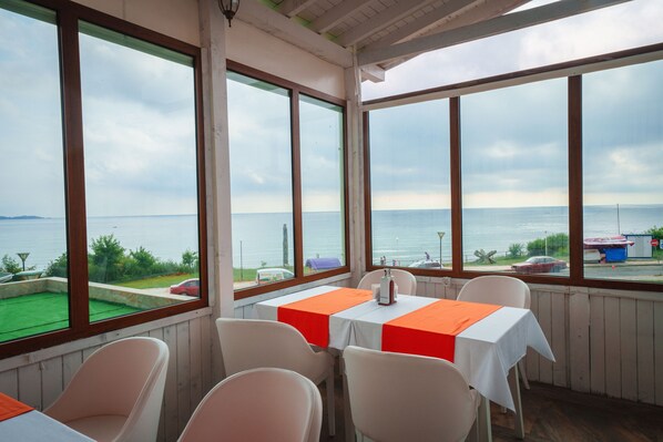 Un comedor con vistas al mar, con mesas cubiertas con manteles anaranjados y sillas blancas.