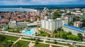 A coastal cityscape with a prominent hotel featuring multiple floors, a swimming pool, and a view of the sea. - Hotel Perla Beach Luxury (Primorsko)