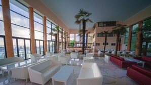 A spacious lobby with white and red sofas, a coffee table, and a palm tree. - Hotel Perla Beach Luxury (Primorsko)