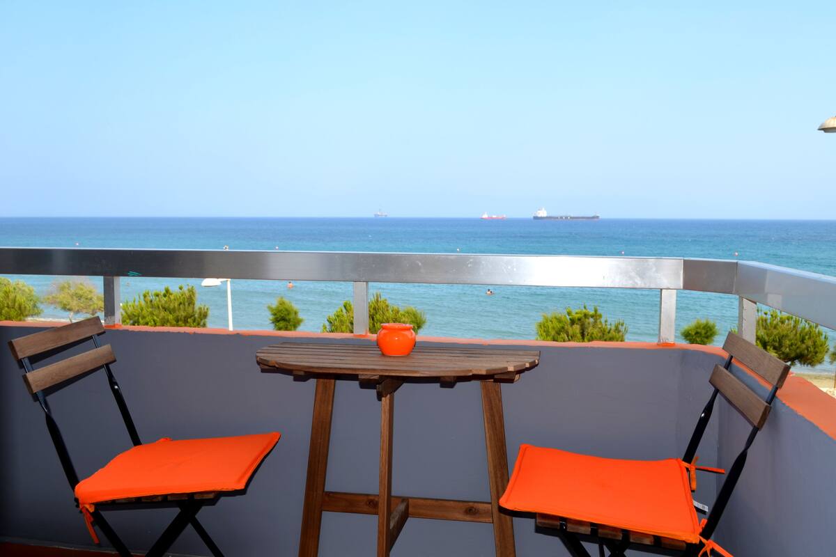 A balcony with two wooden chairs and a small table, overlooking the sea.