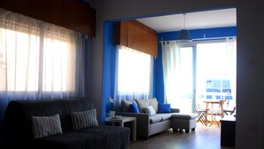 A living room with a sofa, a coffee table, and a dining area with chairs and a table. - Panoramic Blue (Limassol)