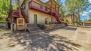 A two-story building with a red balcony, a front door, and a small front yard. - Deer Crossing: Soak, Stargaze, Relax (Ruidoso)