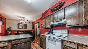 A kitchen with wooden cabinets, a white stove, and a dining area with chairs. - Deer Crossing: Soak, Stargaze, Relax (Ruidoso)