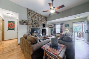 A living room with a stone fireplace, leather sofas, a ceiling fan, and a large window.