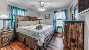 A bedroom with a bed, nightstands, a dresser, a ceiling fan, and a window with curtains. - Deer Crossing: Soak, Stargaze, Relax (Ruidoso)