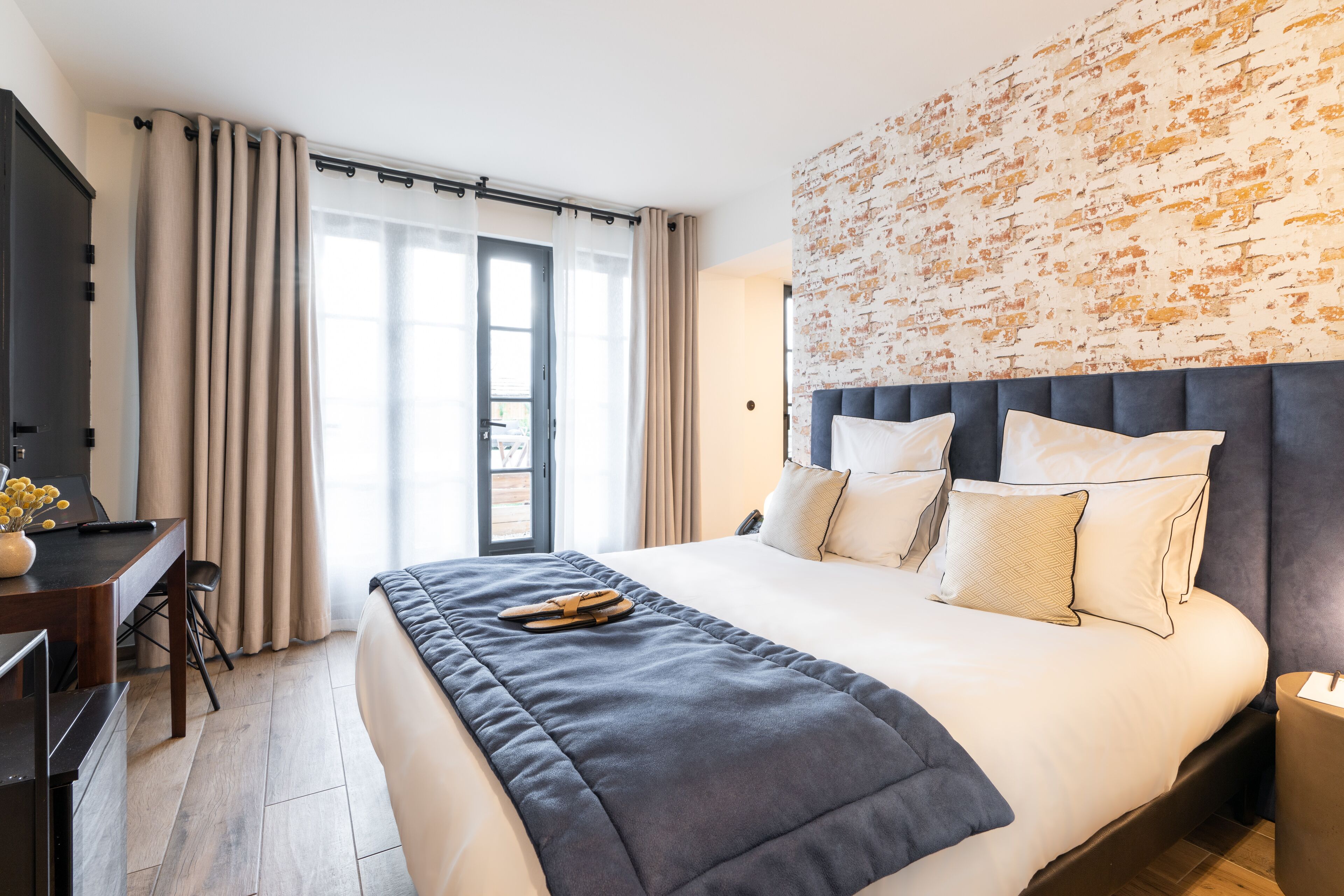 Camera d'albergo moderna con un letto grande, una scrivania con una sedia e vista sull'esterno tramite una porta scorrevole.