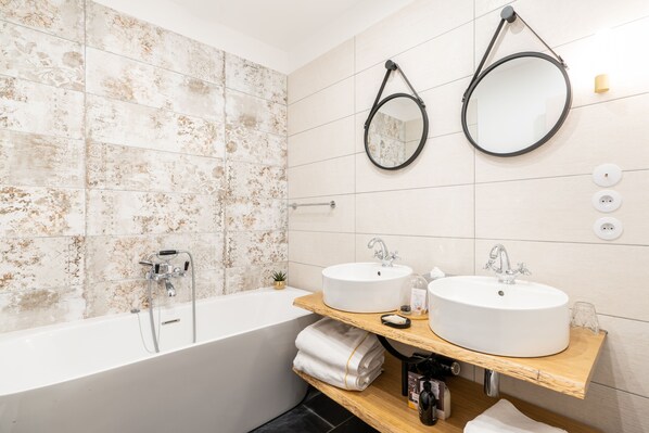 Un baño moderno con dos lavamanos, una bañera y dos espejos fijos en la pared.