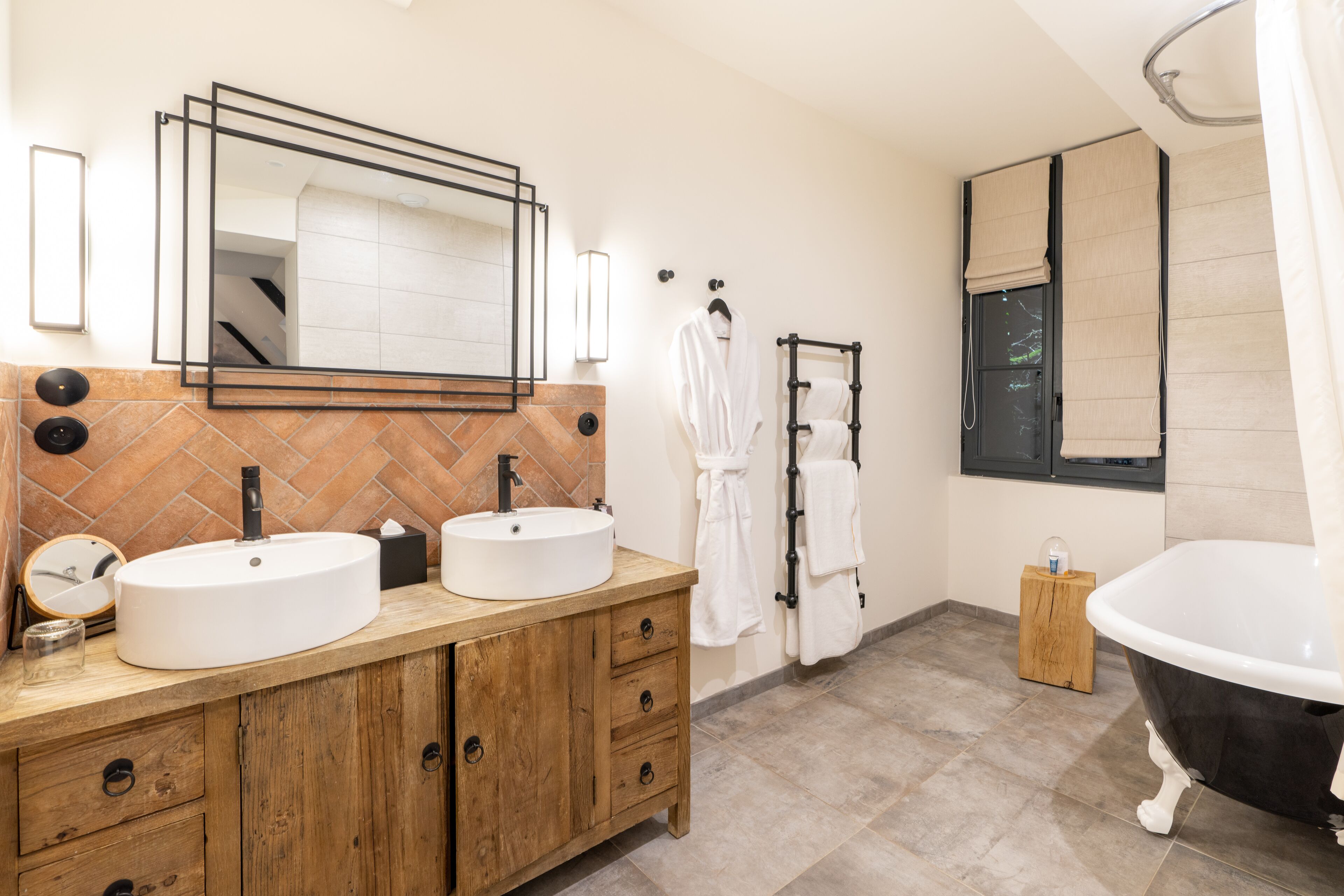 Une salle de bain moderne avec un meuble-lavabo en bois, deux vasques, un grand miroir, une baignoire sur pieds et une fenêtre offrant une belle vue.