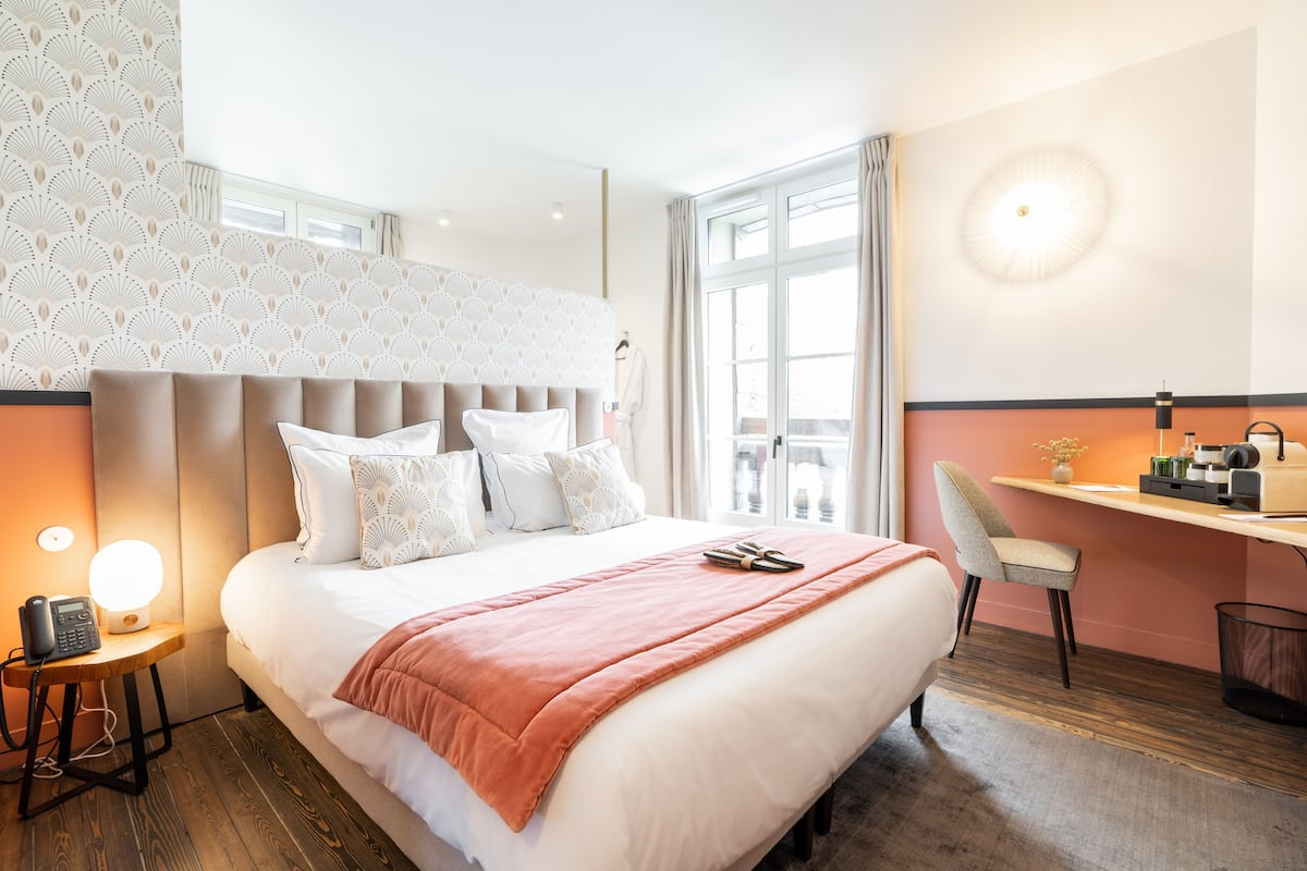 A hotel room with a large bed, a desk, a chair, and a telephone on a side table.