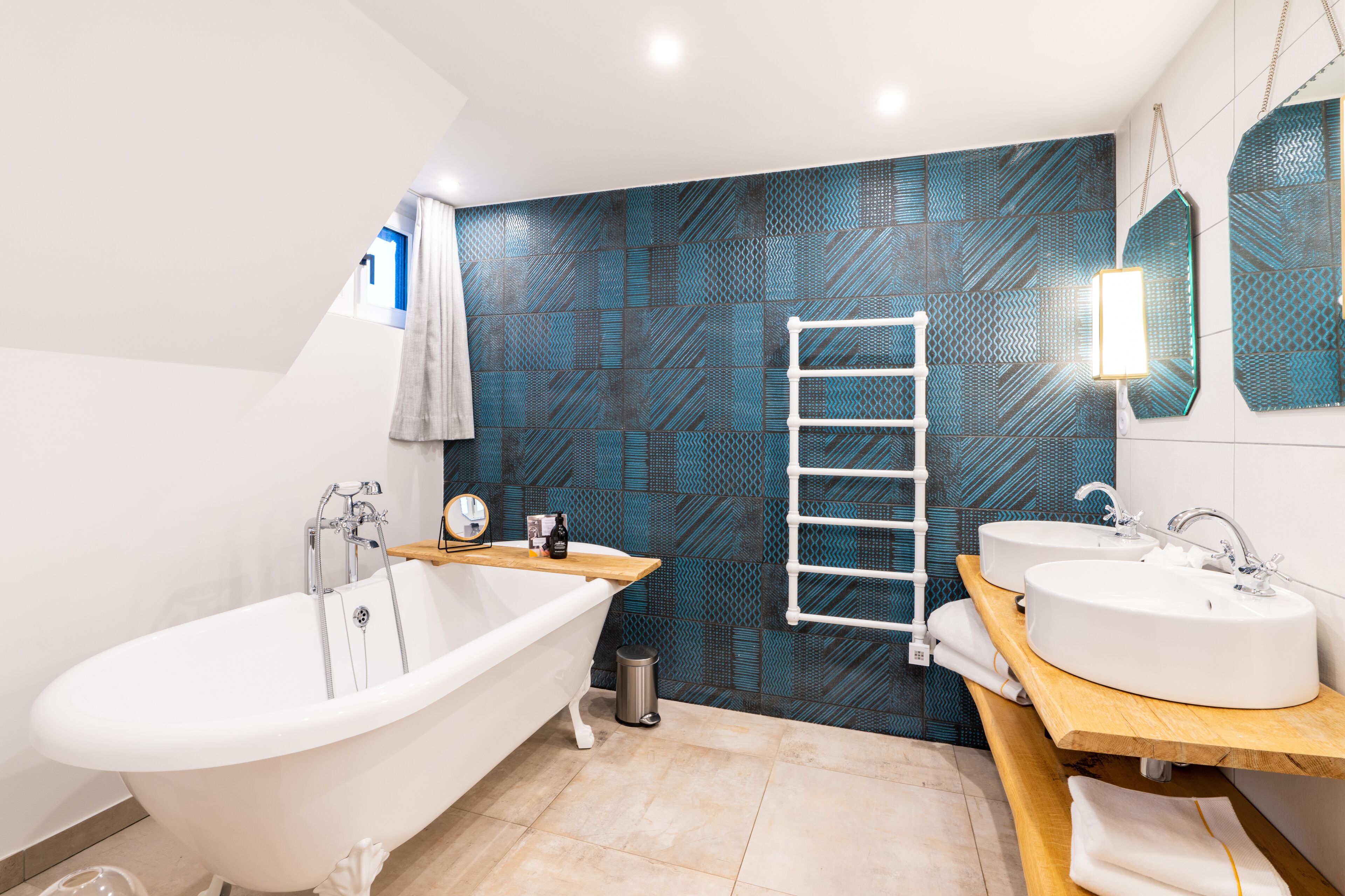 Un baño moderno con una bañera independiente, dos lavamanos, un mueble de tocador de madera, un perchero para toallas y un revestimiento de pared con diseño.