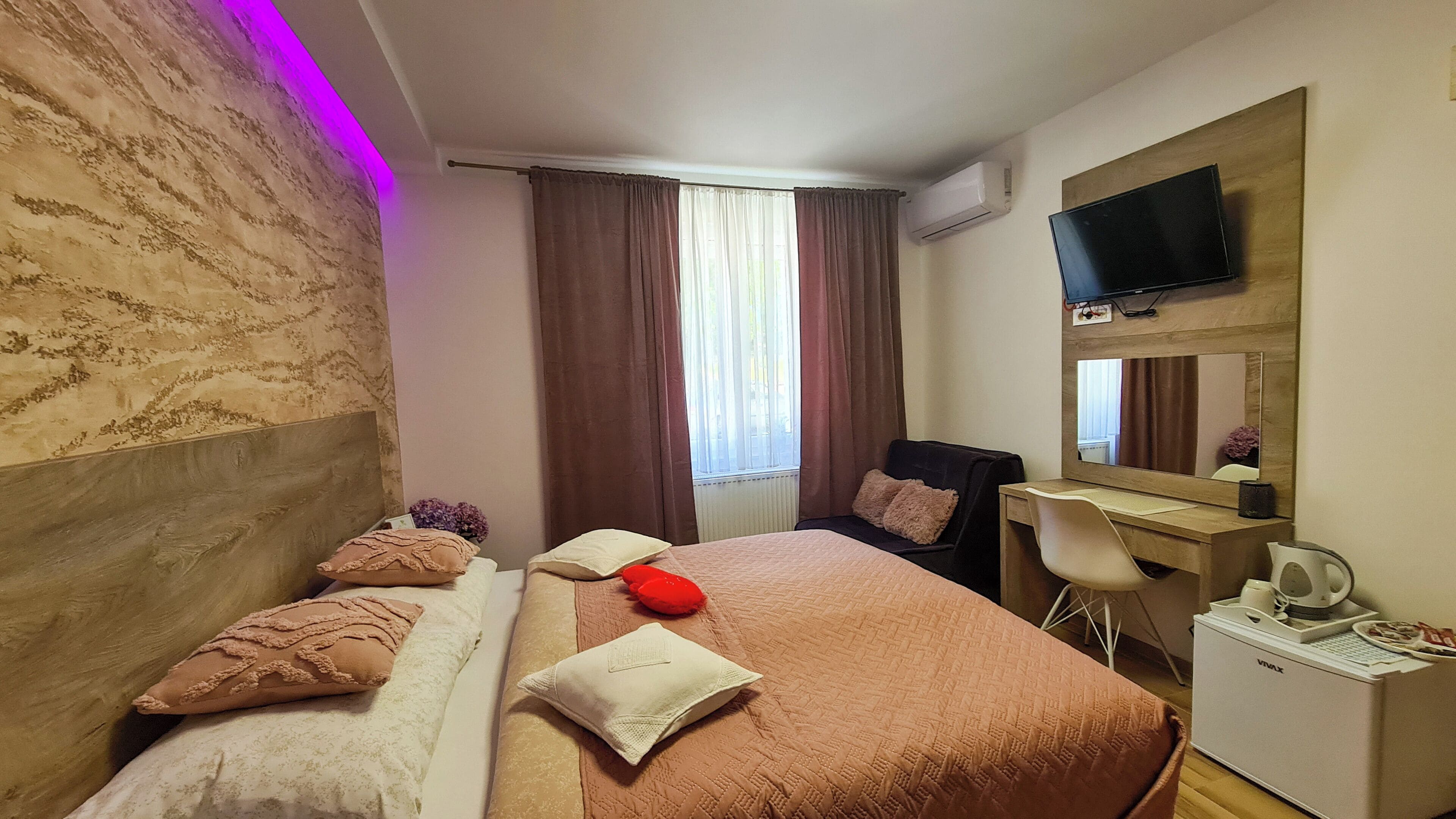 A hotel room with a bed, a desk, a chair, a TV, and an air conditioning unit.