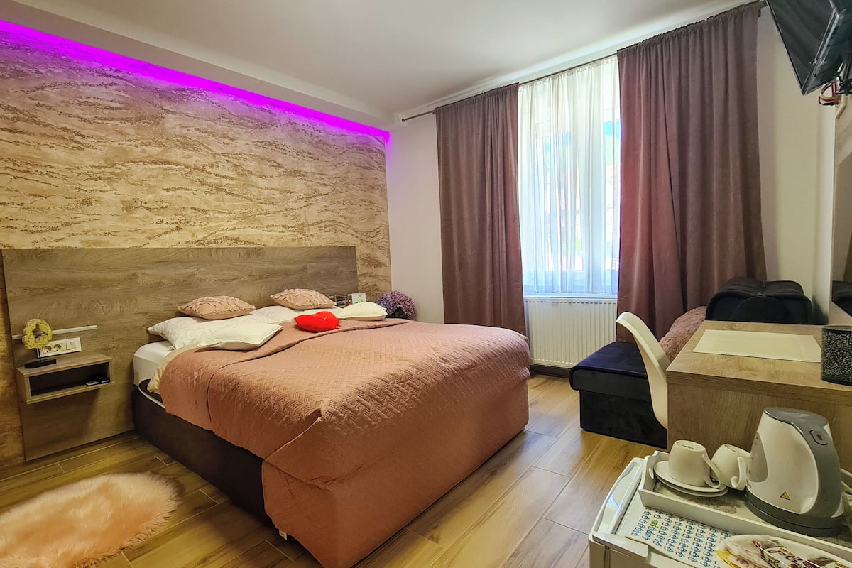 A modern hotel room with a large bed, a desk, and a mirror.