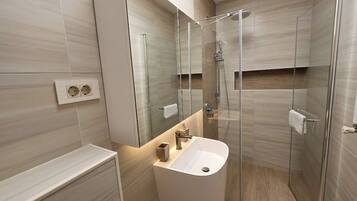 A modern bathroom with a glass-enclosed shower, a white sink, and a mirror above it.