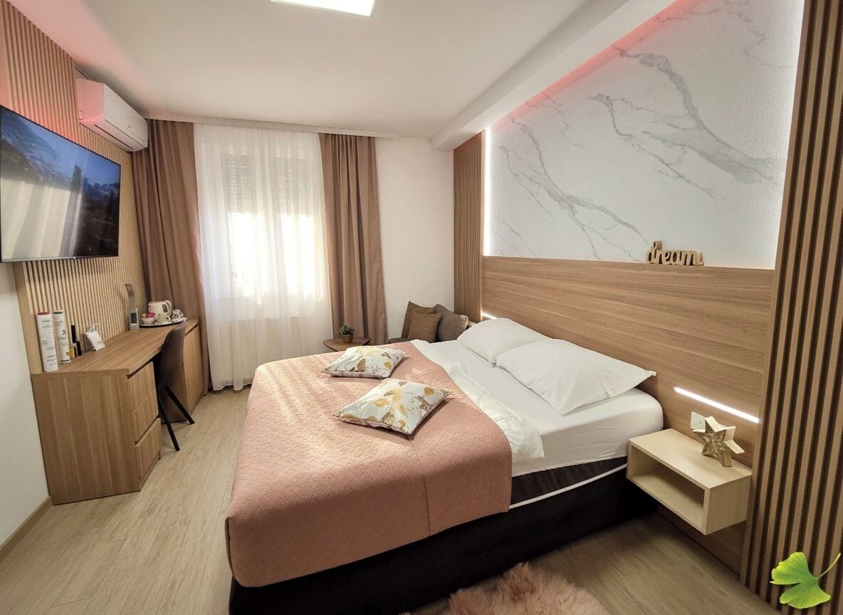 A modern hotel room with a bed, a desk, a TV, and a marble wall.