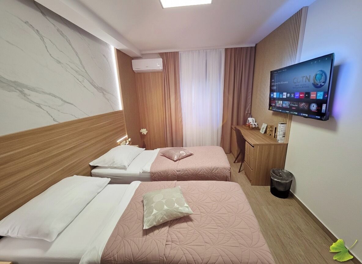 Quarto de hotel com duas camas, uma escrivaninha, uma TV e um aparelho de ar condicionado.