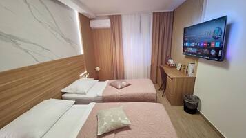 Quarto de hotel com duas camas, uma escrivaninha, uma TV e um aparelho de ar condicionado.