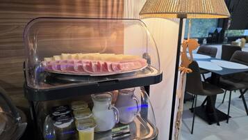 Un buffet pour le petit-déjeuner avec un présentoir en verre contenant du pain tranché, du beurre et diverses garnitures.