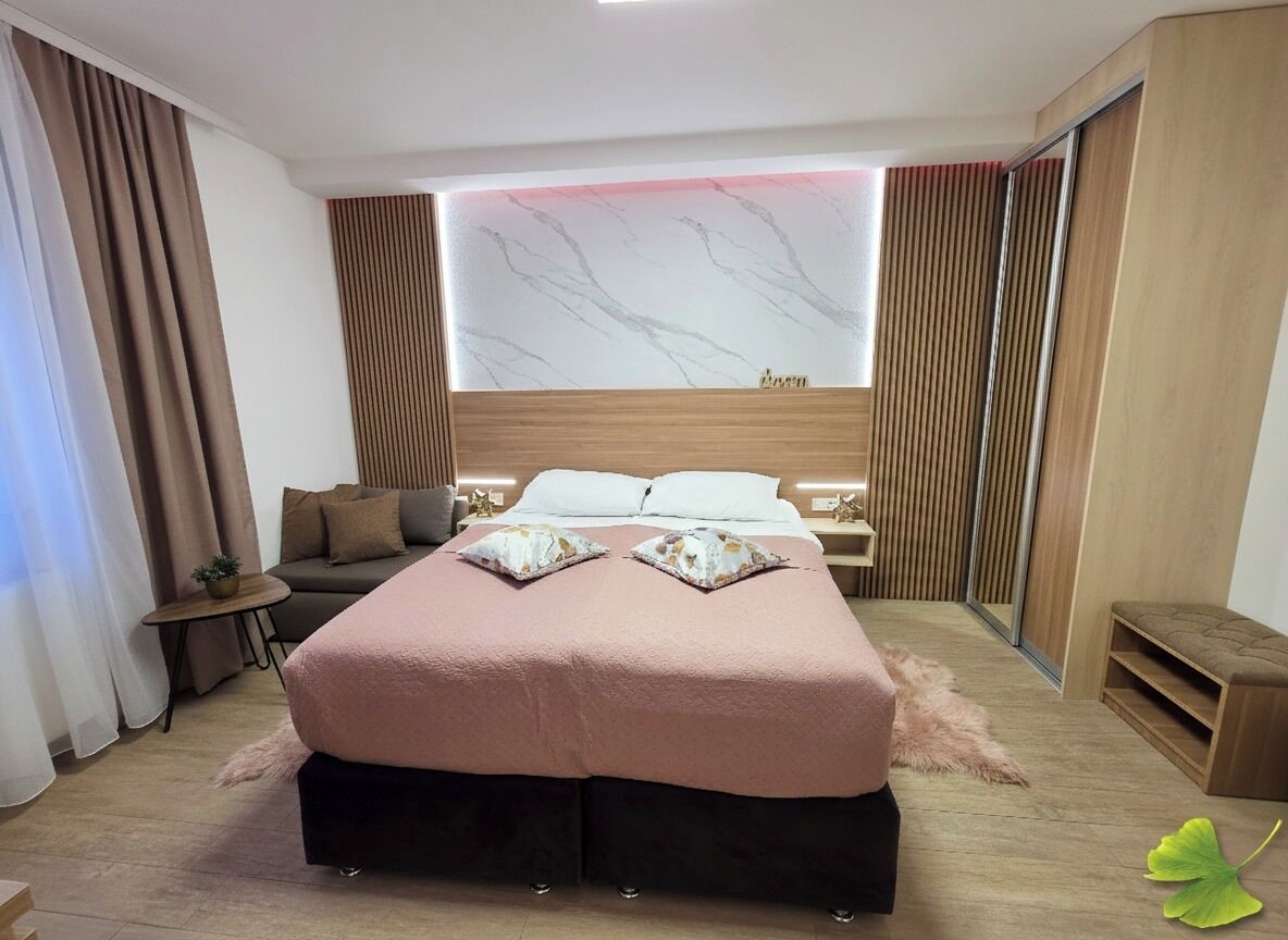 A modern hotel room with a large bed, a sofa, a small table, and a mirror.