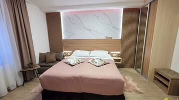 A modern hotel room with a large bed, a sofa, a small table, and a mirror.