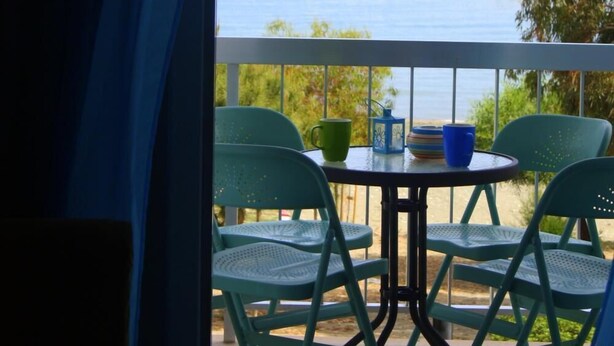 Un balcone con vista sul mare, con un tavolo e sedie e una barca a vela in lontananza.