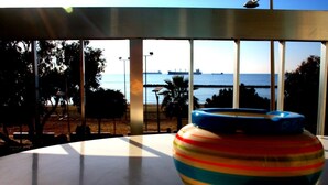 Vista da una stanza con ampie finestre su una spiaggia e una nave all'orizzonte.