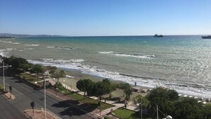 Una strada costiera con una spiaggia alla destra, un percorso pedonale e un cielo azzurro limpido.