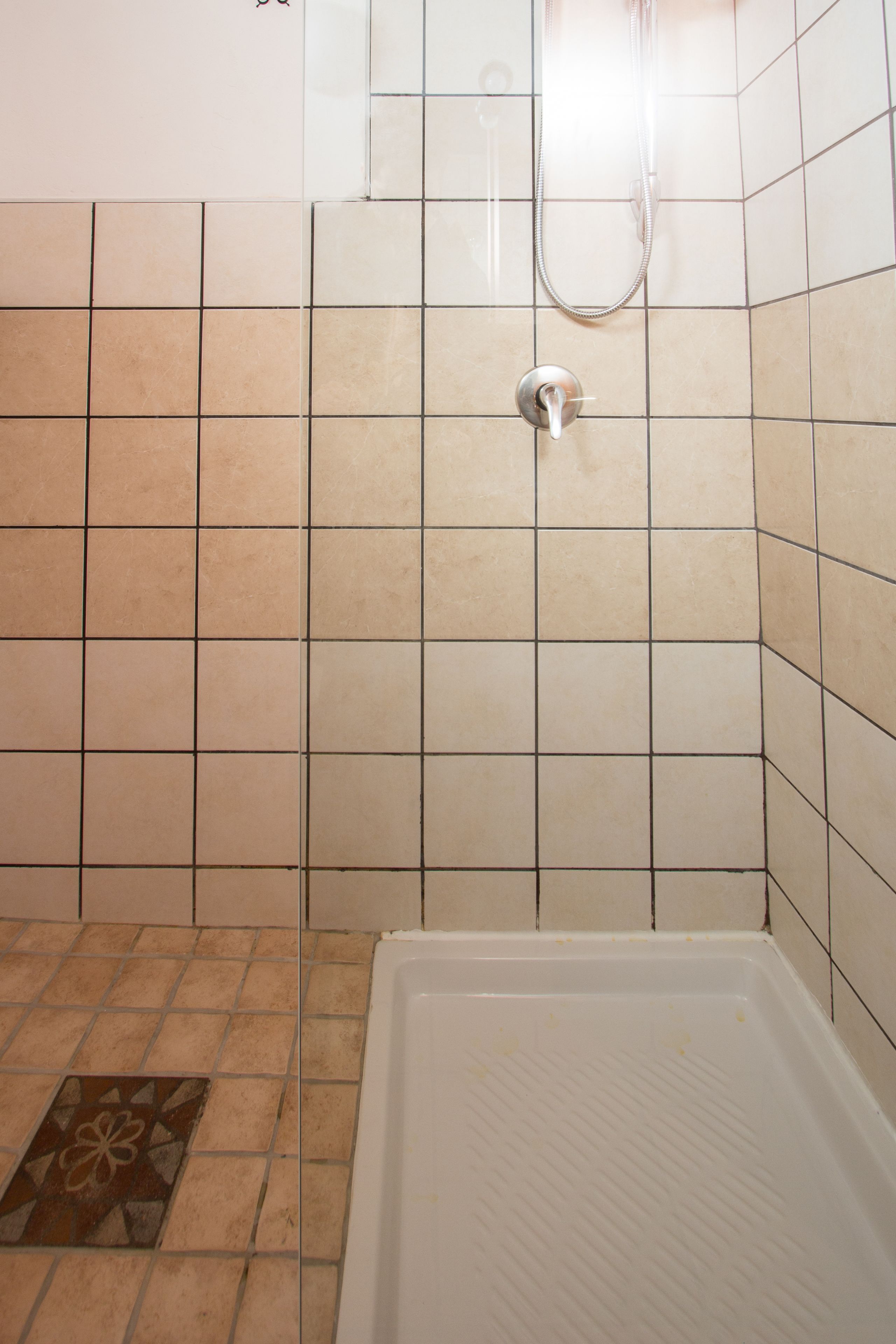 A bathroom with beige tiles, a shower, and a white bathtub.