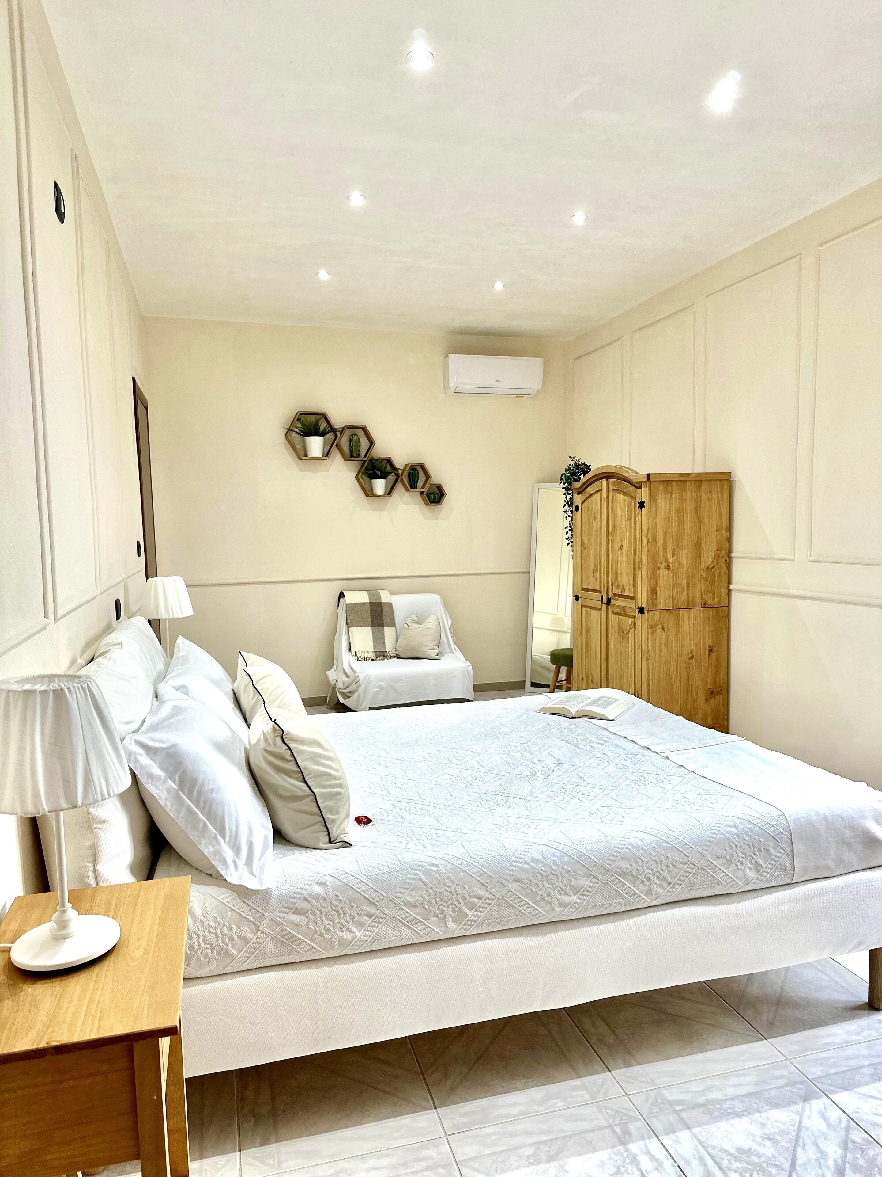 Un dormitorio con cama, mesita de noche, lámpara, silla, armario y decoración en la pared.