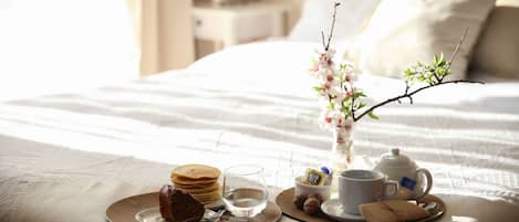 A neatly arranged breakfast setup on a bed with a vase of flowers, a teapot, and a cup.