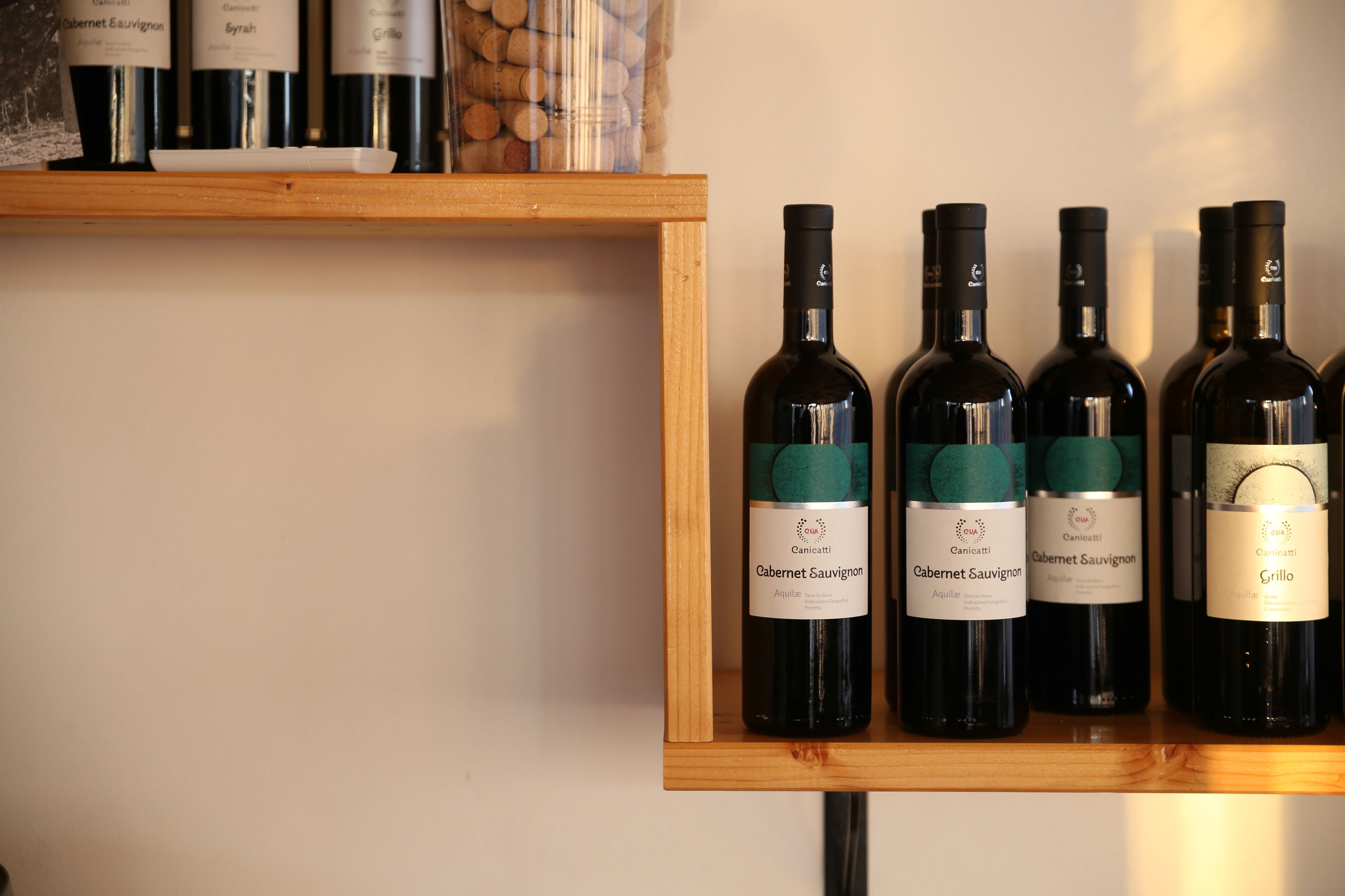 A wooden shelf with several wine bottles labeled "Cabernet Sauvignon" and "Grillo".