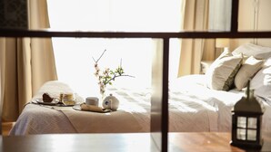 A neatly made bed with white linens, a bedside table with a small lantern, and a window with curtains. - B&B Eyexei Domus (Agrigento)