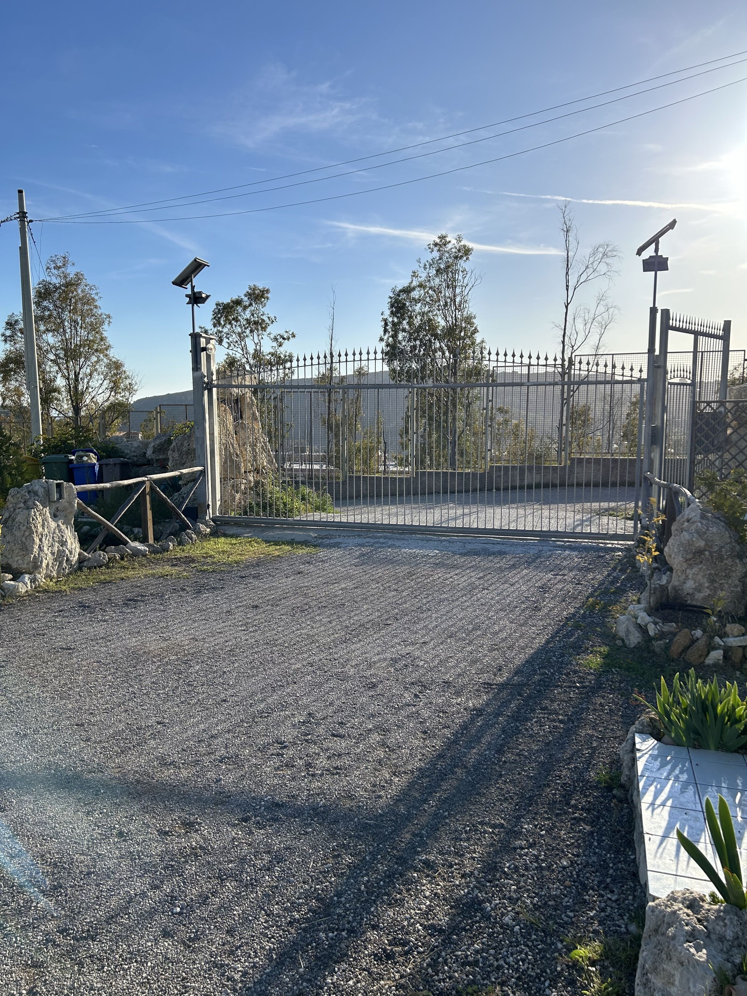 A gated entrance with a metal fence, gravel path, and a solar-powered security light.