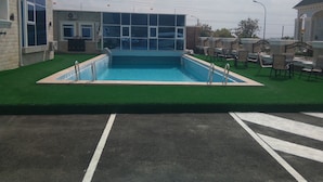 Une piscine rectangulaire à l’intérieur bleu, entourée de gazon artificiel vert.
