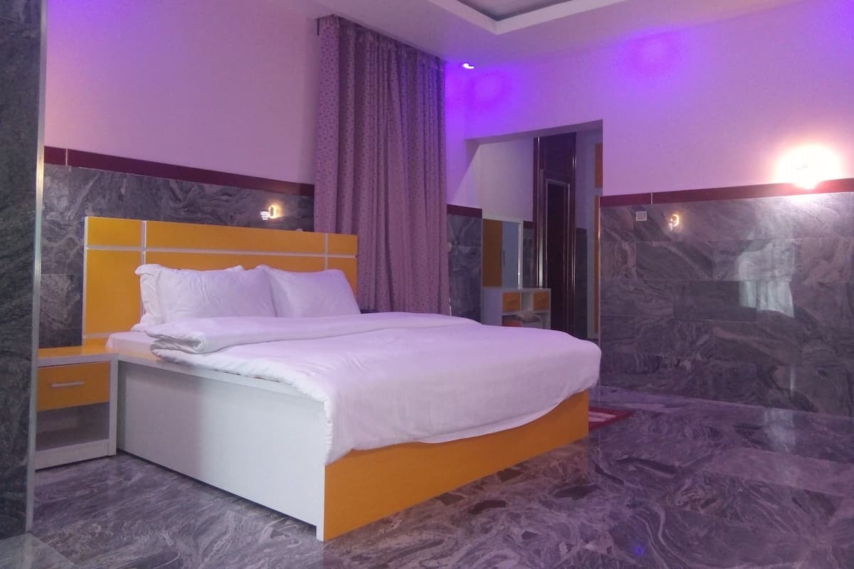 A modern hotel room with a marble floor, a bed with a white and orange headboard, a nightstand, and a large mirror.