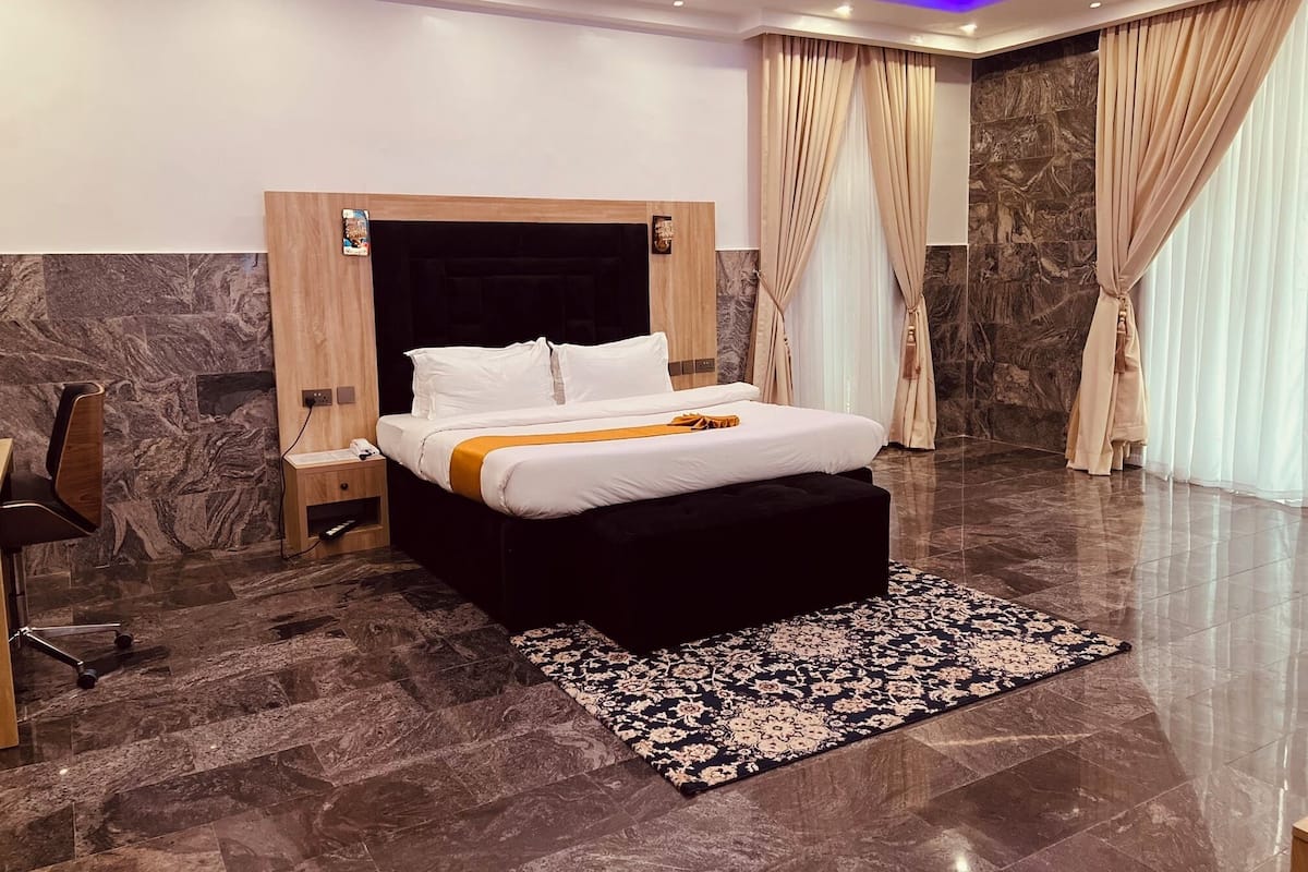 A modern hotel room with a large bed, a nightstand, a chair, and a marble floor.