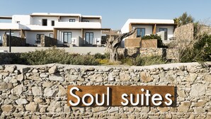 Een bord met de tekst 'Soul suites' voor een stenen muur, met moderne witte gebouwen op de achtergrond.