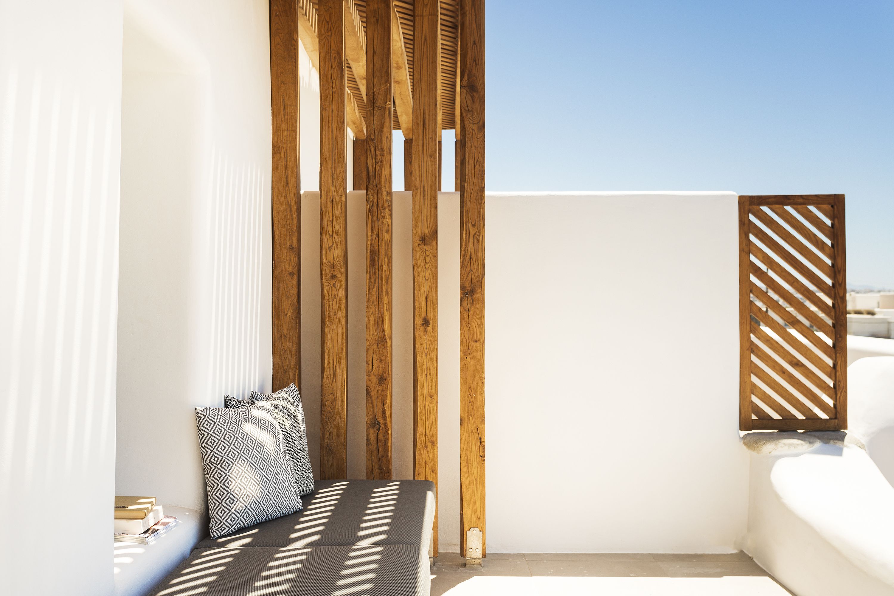 A balcony with a wooden partition, a white wall, and a white sofa with patterned cushions.
