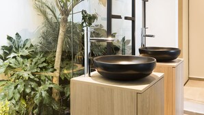 Een moderne badkamer met twee zwarte wasbakken, houten kastjes en een groot raam met uitzicht op kamerplanten.