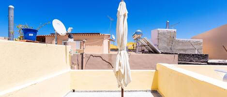 A rooftop terrace with a satellite dish, a potted plant, and a white umbrella.
