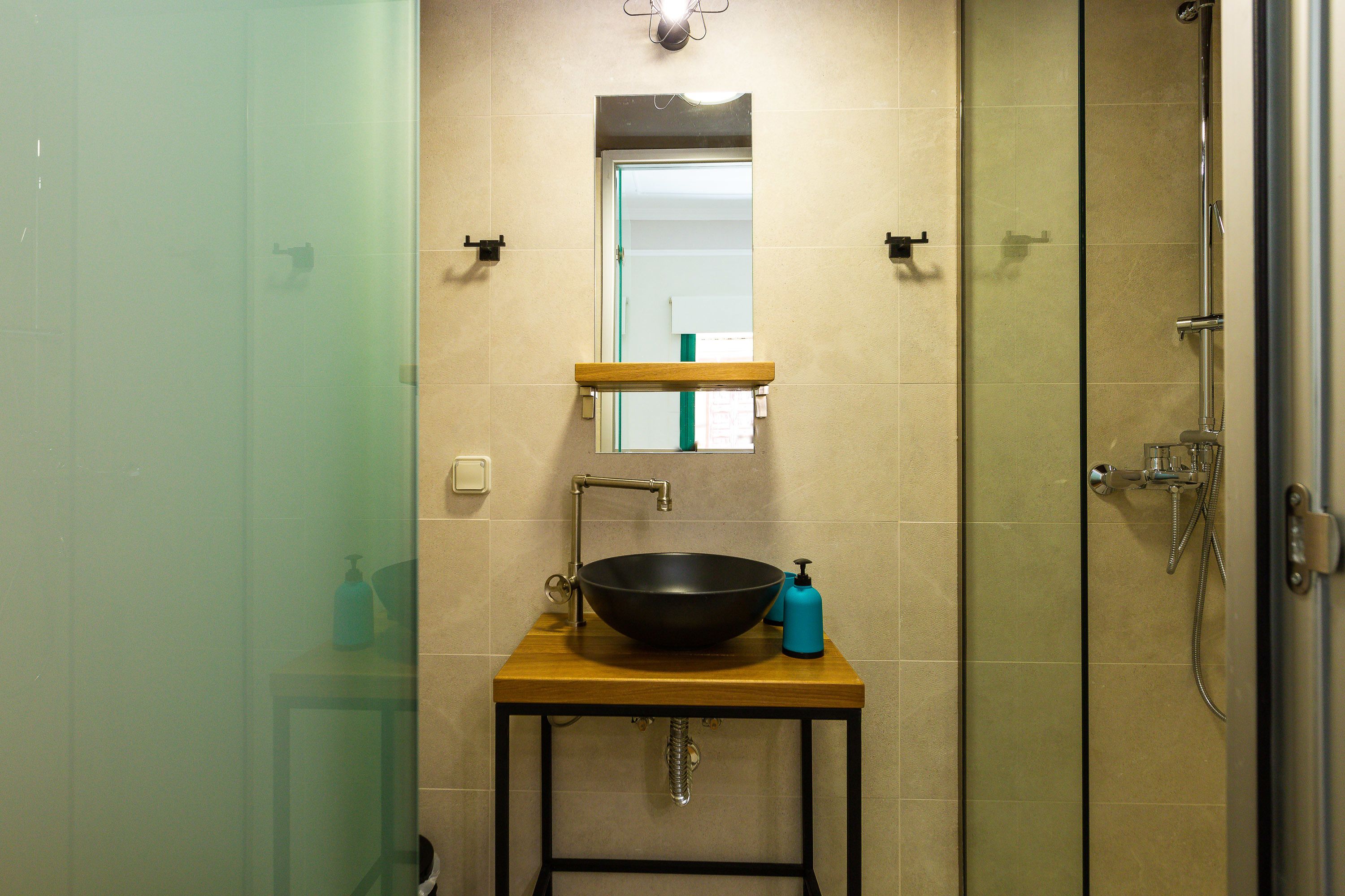 A bathroom with a wooden vanity, a black vessel sink, a mirror, and a shower enclosure.