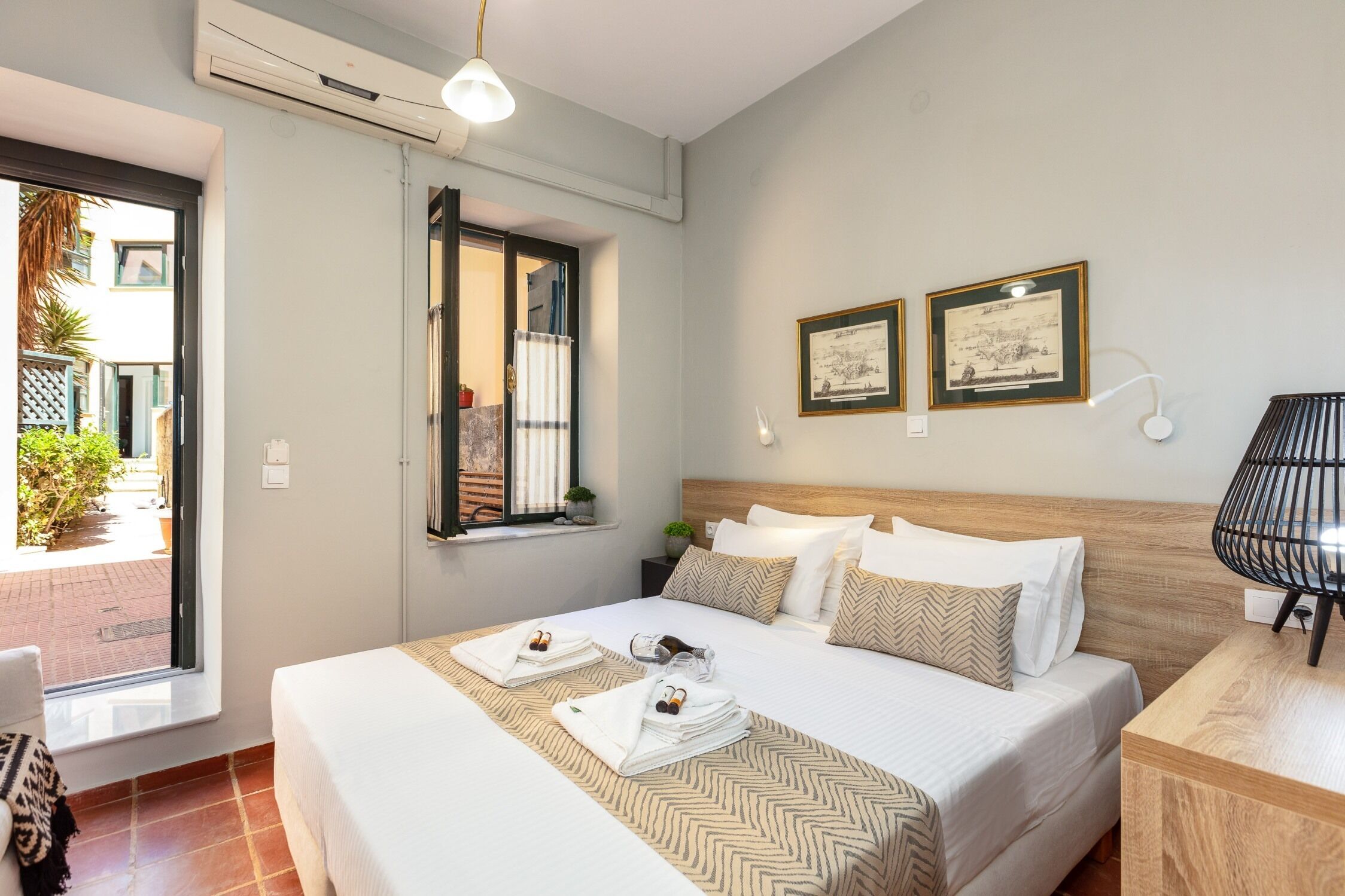 A hotel room with a bed, a window, a nightstand, and a wall-mounted lamp.