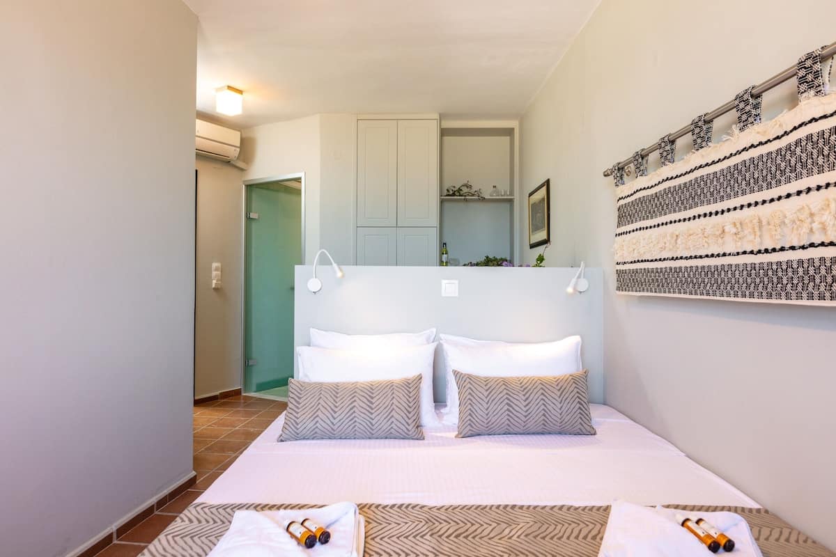 A bedroom with a bed, pillows, a headboard, a wall-mounted shelf, and a door.