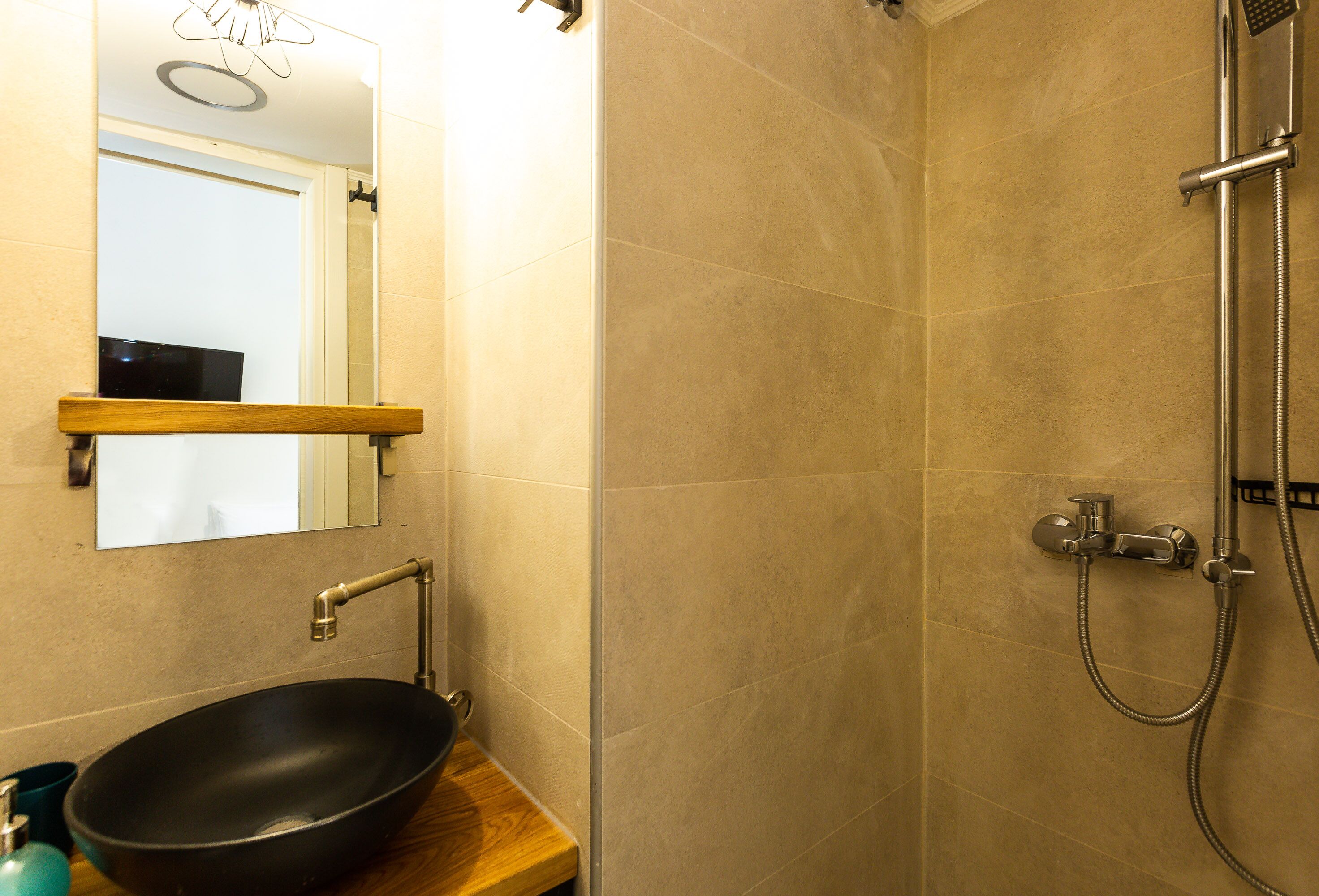 A bathroom with a wooden vanity, a black vessel sink, a mirror, and a shower with a handheld showerhead.
