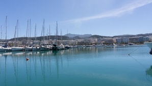 A marina with multiple sailboats docked, a calm water body, and a cityscape with buildings in the background. - Ink Hotels House of Europe (Rethymno)
