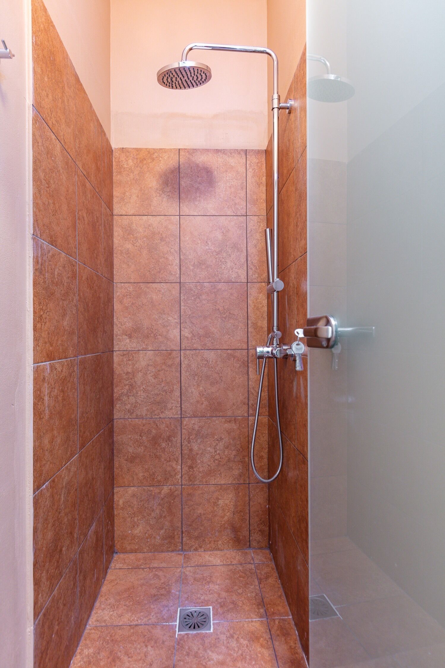 A small, tiled shower stall with a handheld showerhead and a wall-mounted faucet.
