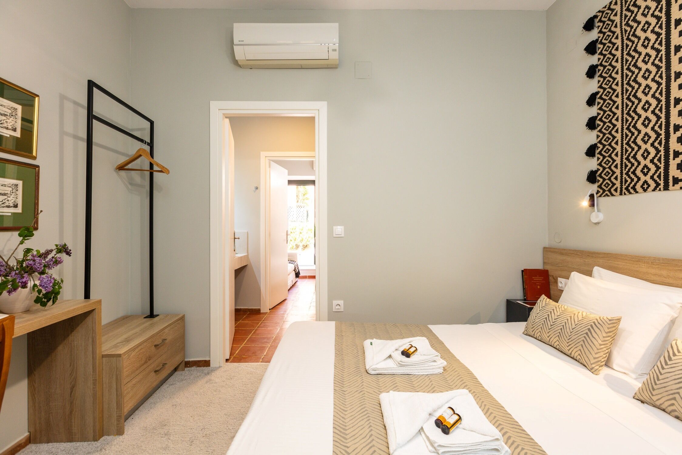 Ein Hotelzimmer mit Bett, Nachttischen, Schreibtisch, Stuhl, Kleiderhaken und einer Wand-Klimaanlage.