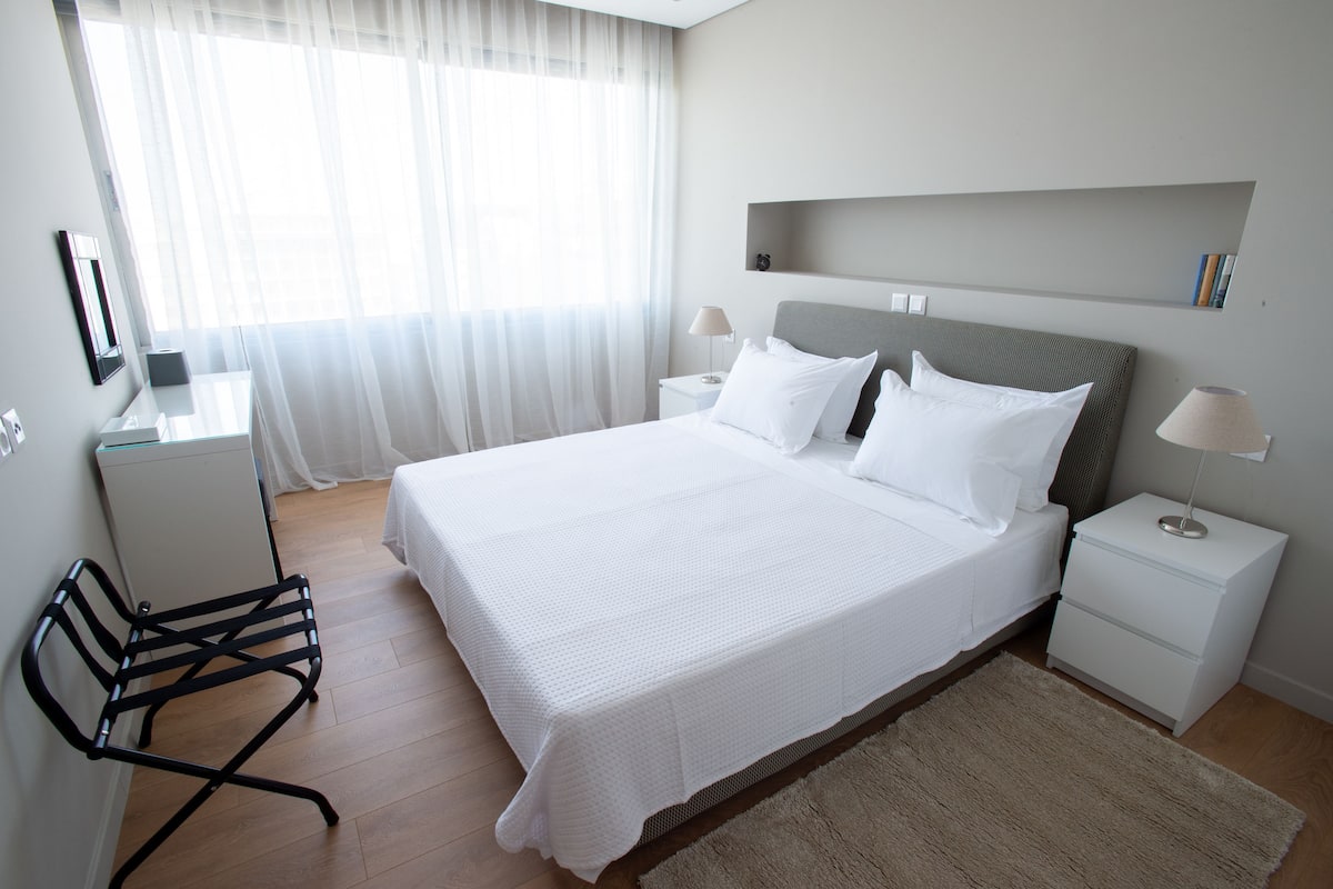 Quarto bem arrumado com uma cama grande, mesas de cabeceira, uma cadeira e uma escrivaninha.