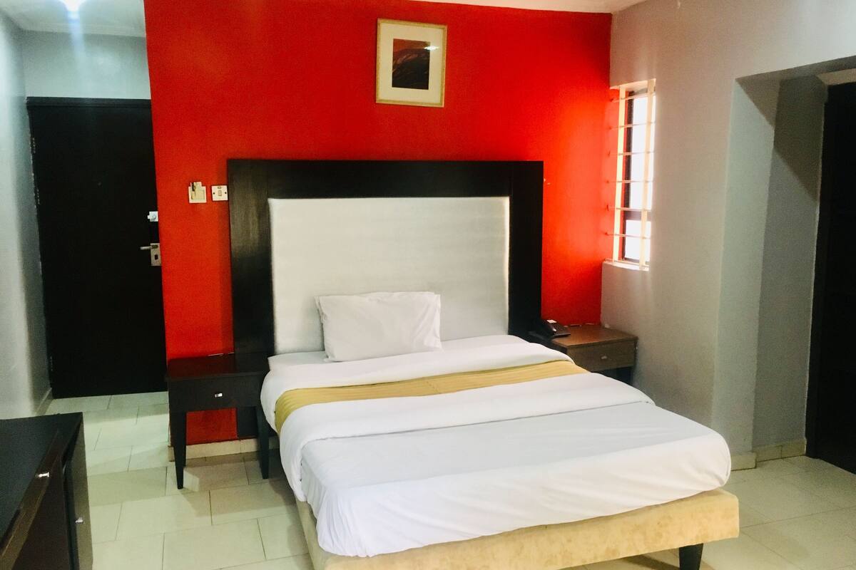 A hotel room with a large bed, a bedside table, a nightstand, and a window.