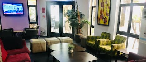 A lobby with a red sofa, a green patterned sofa, a small table with a plant, and a television on the wall.